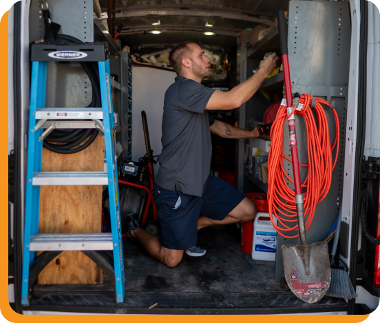 Technician in a Pro-Tec uniform adjusting settings on a gray HVAC unit.