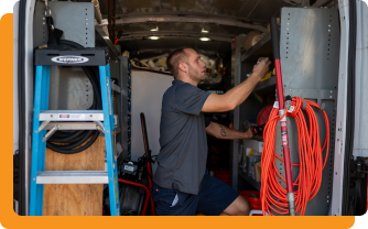 Technician in a Pro-Tec uniform adjusting settings on a gray HVAC unit.