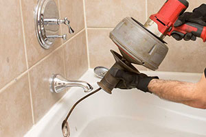 Plumber using a drain snake in a bathtub drain