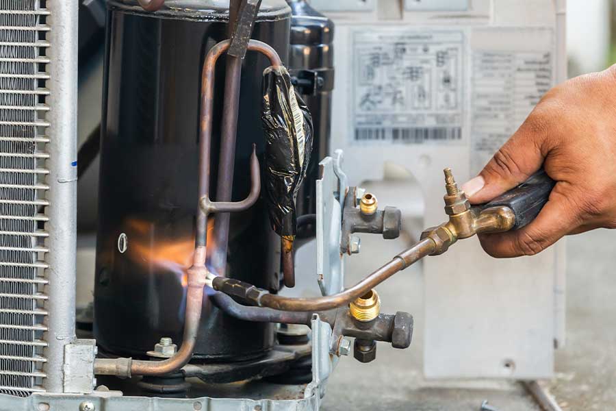 Technician repairing AC unit in Estero FL with welding torch