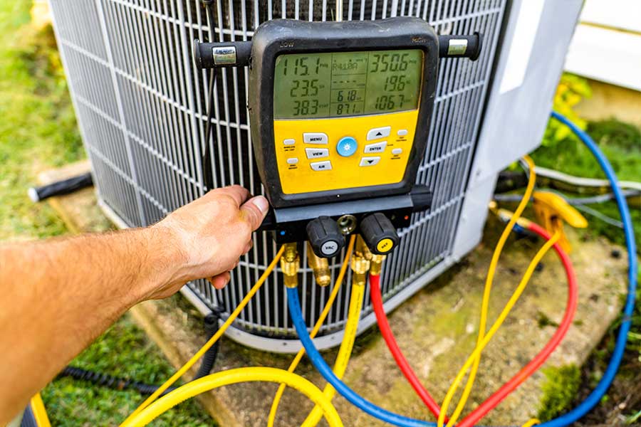 Outdoor commercial HVAC unit being tested with refrigerant hoses and diagnostic gauges