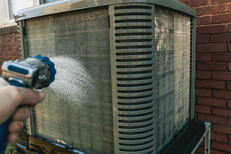 Technician rinsing an outdoor AC unit during coil cleaning service in Naples, FL