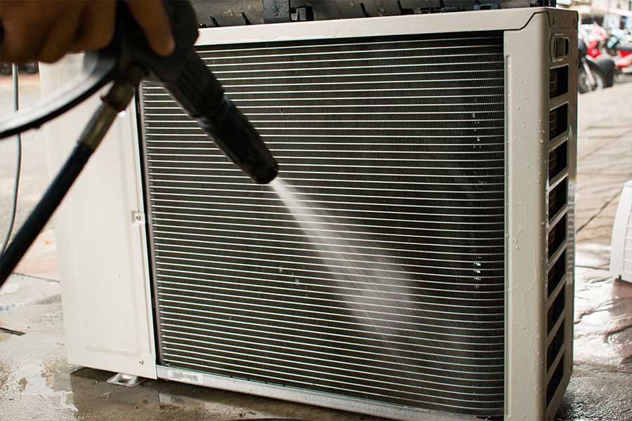 Technician rinsing buildup from a commercial condenser coil during cleaning service