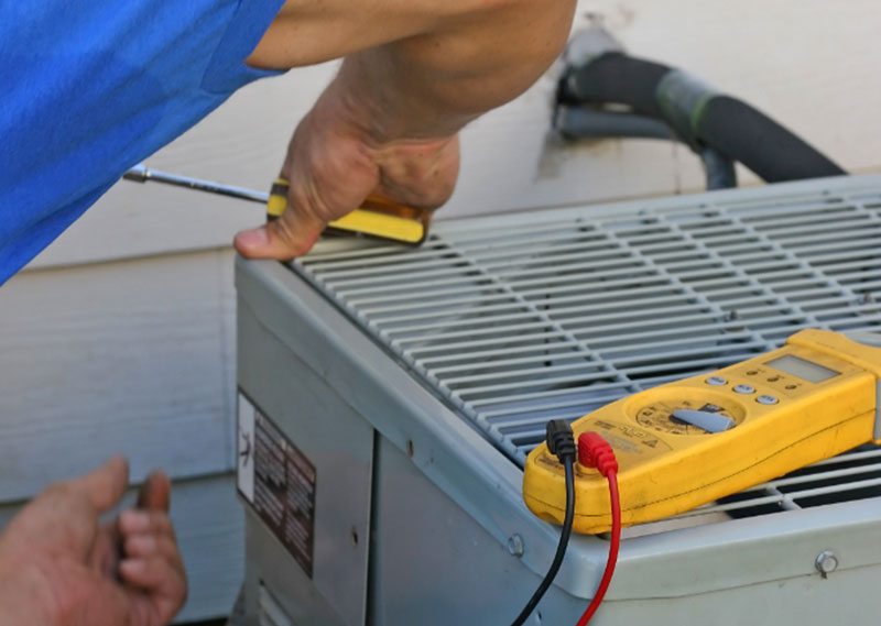 Technician checking refrigerant lines on a commercial HVAC unit with a digital meter