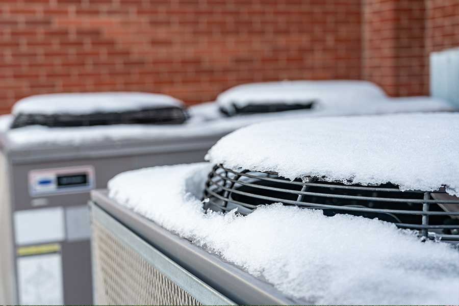Snow-covered commercial HVAC units showing conditions that may lead to refrigerant leak recharge service